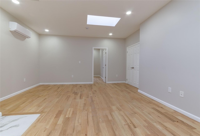 unfurnished room featuring an AC wall unit, light hardwood / wood-style flooring, and a skylight