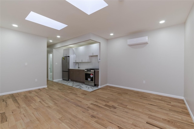 unfurnished living room with a skylight, light hardwood / wood-style flooring, an AC wall unit, and sink