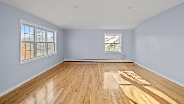 empty room featuring vaulted ceiling, a healthy amount of sunlight, light hardwood / wood-style flooring, and baseboard heating