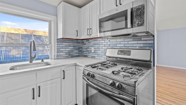 kitchen with sink, light wood-type flooring, white cabinetry, light stone counters, and stainless steel appliances