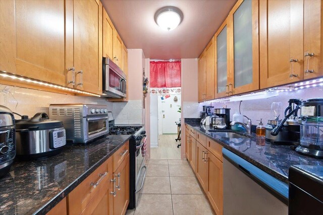 kitchen featuring appliances with stainless steel finishes, tasteful backsplash, dark stone counters, sink, and light tile patterned flooring