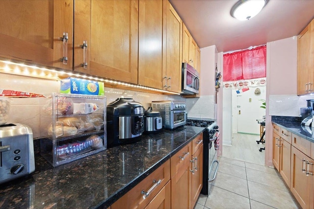 kitchen featuring electric range, decorative backsplash, light tile patterned flooring, and dark stone counters