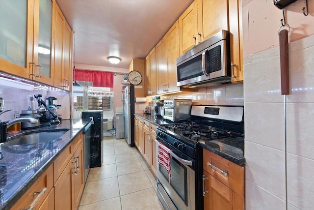 kitchen featuring dark stone countertops, sink, light tile patterned floors, and stainless steel appliances