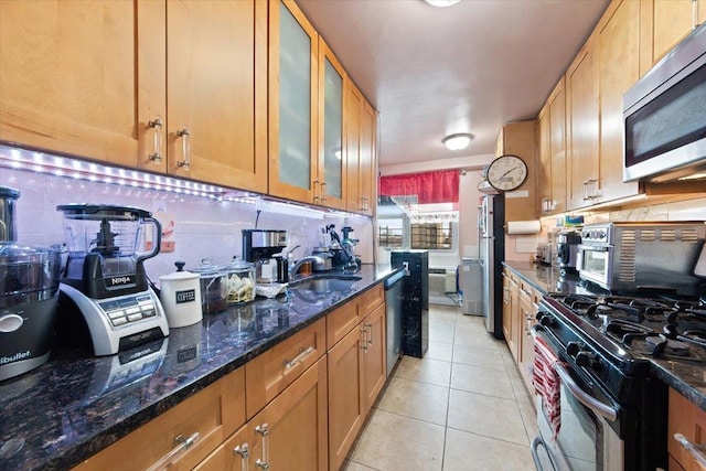 kitchen featuring sink, stainless steel appliances, backsplash, dark stone counters, and light tile patterned floors