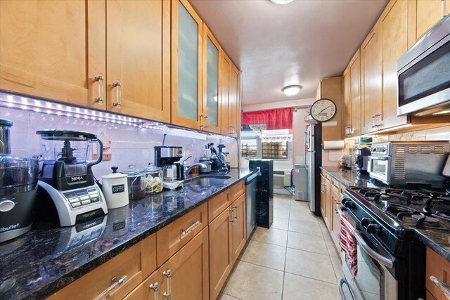 kitchen featuring sink, stainless steel appliances, backsplash, dark stone counters, and light tile patterned floors