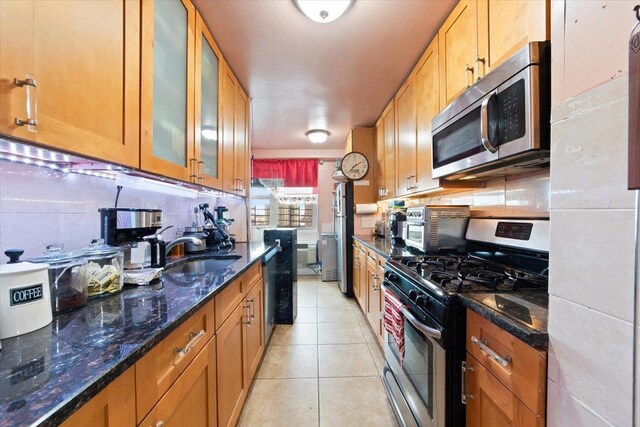 kitchen with sink, dark stone countertops, light tile patterned floors, appliances with stainless steel finishes, and tasteful backsplash