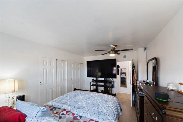 bedroom with ceiling fan, light hardwood / wood-style floors, and two closets