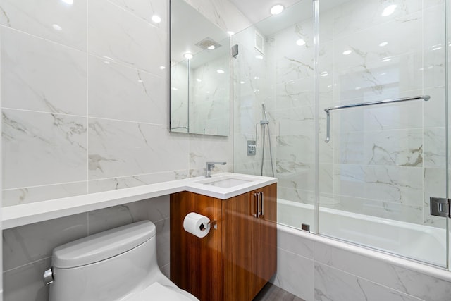 full bathroom with vanity, bath / shower combo with glass door, tile walls, and toilet