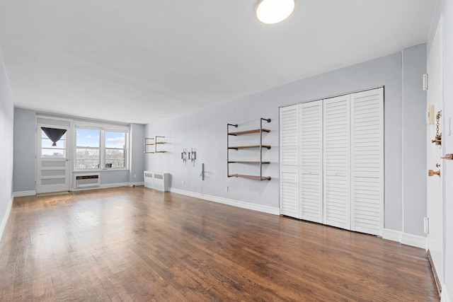 unfurnished living room featuring a wall mounted air conditioner, radiator heating unit, and dark hardwood / wood-style floors