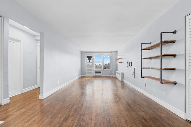 unfurnished living room with a wall unit AC, radiator, and dark wood-type flooring