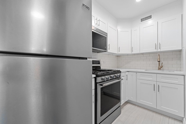 kitchen with white cabinets, appliances with stainless steel finishes, tasteful backsplash, and sink