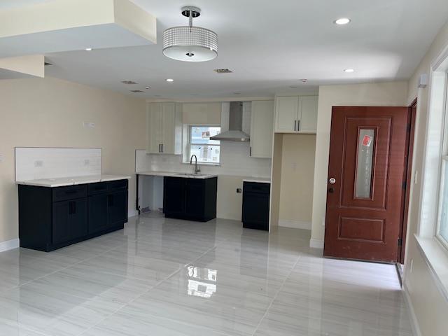 kitchen featuring white cabinets, wall chimney exhaust hood, and sink