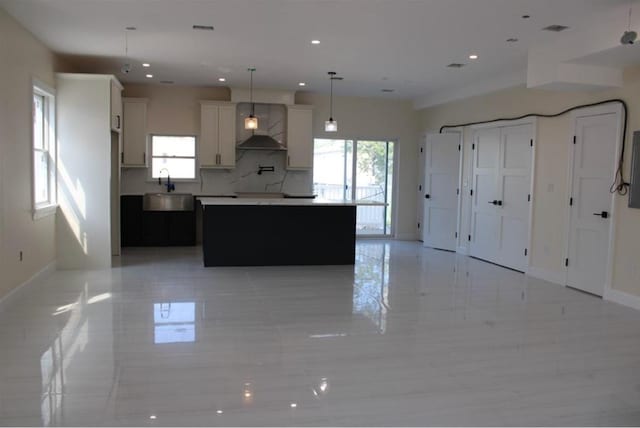 kitchen with sink, wall chimney exhaust hood, decorative light fixtures, decorative backsplash, and a kitchen island