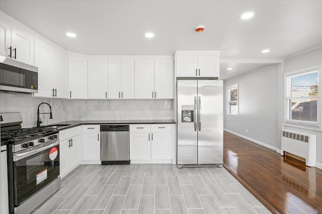 kitchen featuring tasteful backsplash, radiator, stainless steel appliances, sink, and white cabinetry