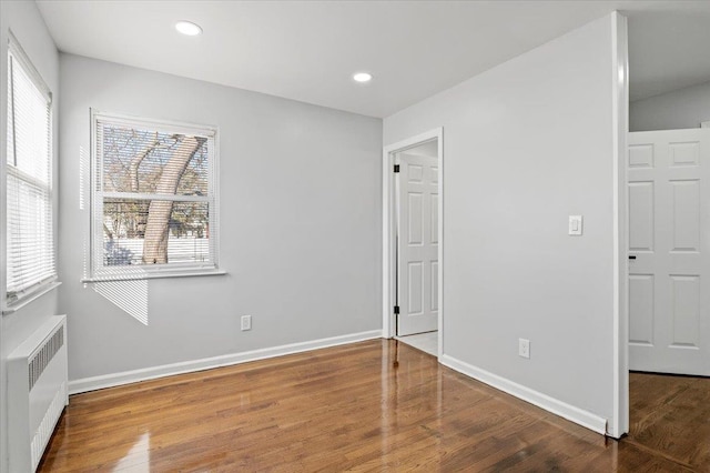 unfurnished bedroom with multiple windows, radiator heating unit, and hardwood / wood-style floors