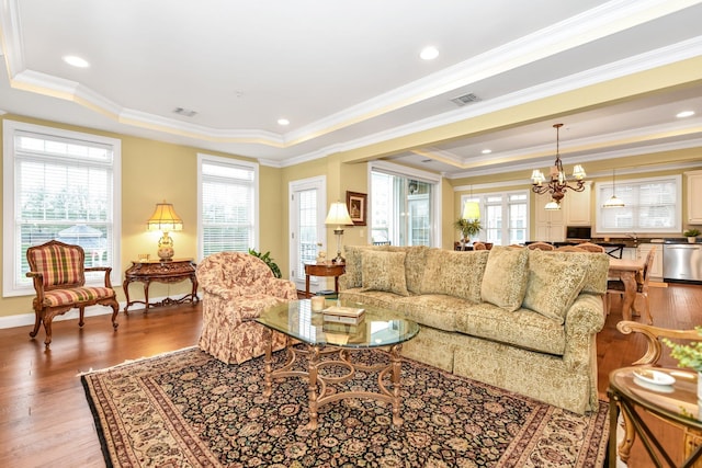 living room featuring hardwood / wood-style flooring, a notable chandelier, a raised ceiling, and ornamental molding