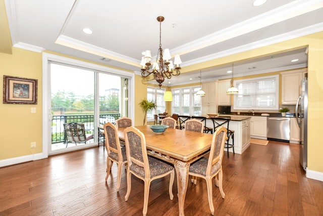 dining area featuring a chandelier, ornamental molding, dark wood-type flooring, and a tray ceiling