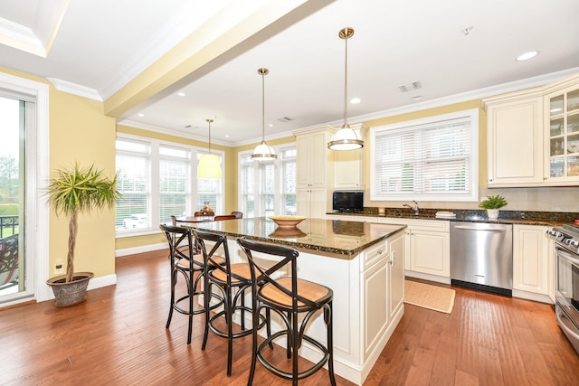 kitchen featuring a center island, hanging light fixtures, stainless steel appliances, dark stone counters, and a kitchen bar