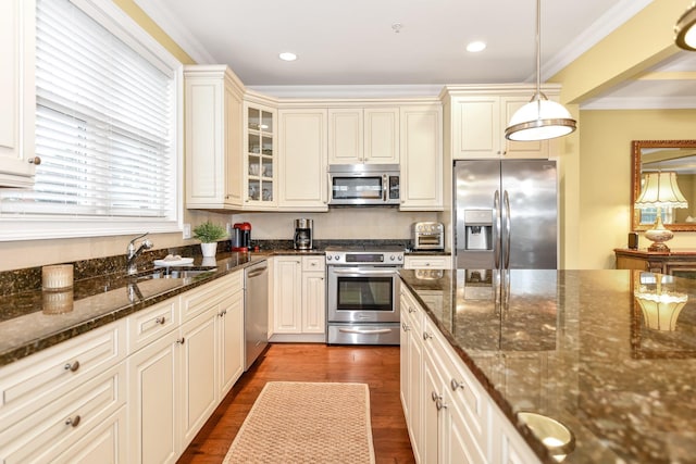 kitchen with dark stone countertops, hanging light fixtures, stainless steel appliances, and sink