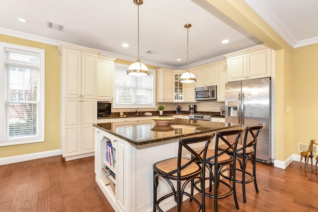 kitchen with appliances with stainless steel finishes, a kitchen breakfast bar, ornamental molding, pendant lighting, and a center island