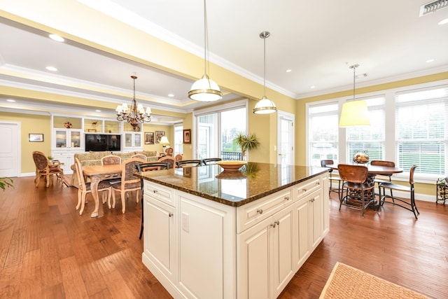 kitchen featuring a kitchen island, crown molding, hanging light fixtures, and dark stone counters