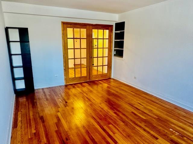 spare room featuring french doors, built in shelves, and hardwood / wood-style floors