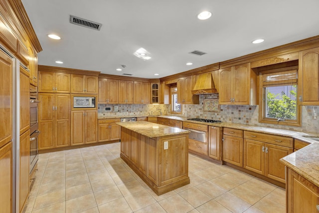 kitchen featuring tasteful backsplash, light stone counters, custom range hood, stainless steel appliances, and a center island