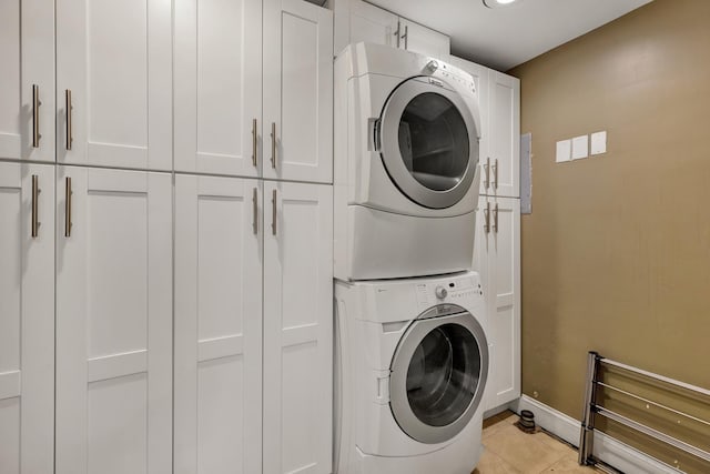 clothes washing area with light tile patterned floors, cabinets, and stacked washer / drying machine