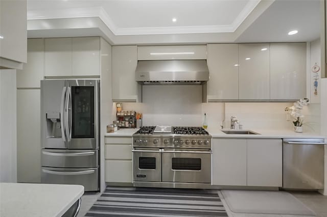 kitchen with appliances with stainless steel finishes, ornamental molding, light countertops, wall chimney range hood, and a sink