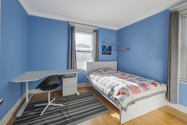 bedroom featuring baseboards, wood finished floors, and crown molding