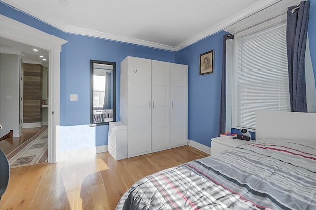 bedroom featuring light wood-style floors, a closet, crown molding, and baseboards