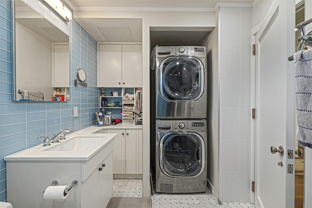 laundry room with stacked washing maching and dryer, laundry area, tile walls, and a sink