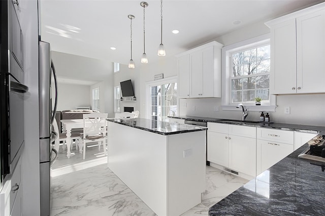 kitchen with sink, a kitchen island, dark stone countertops, decorative light fixtures, and white cabinets