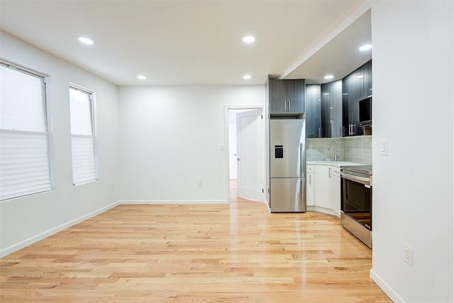 kitchen with appliances with stainless steel finishes, backsplash, light hardwood / wood-style flooring, and sink