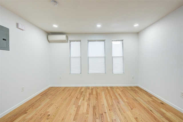 unfurnished room featuring electric panel, a wall mounted air conditioner, and light wood-type flooring