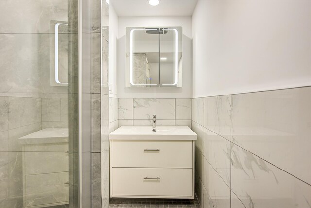 bathroom featuring vanity, a shower with shower door, and tile walls