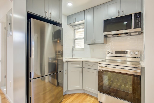 kitchen featuring tasteful backsplash, stainless steel appliances, sink, light hardwood / wood-style flooring, and gray cabinets