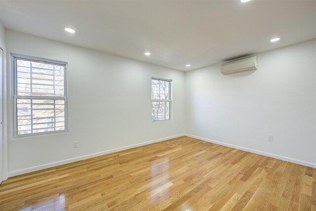 spare room featuring light hardwood / wood-style floors, an AC wall unit, and a wealth of natural light