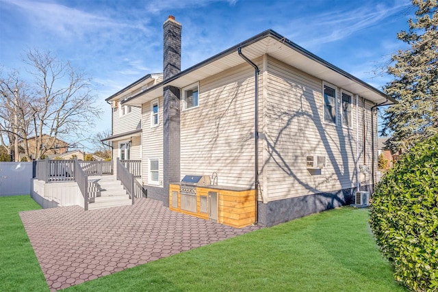 back of house with a wooden deck, cooling unit, exterior kitchen, a patio area, and a lawn