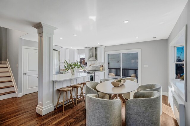 dining room with dark wood-style floors, radiator, ornate columns, stairway, and baseboards