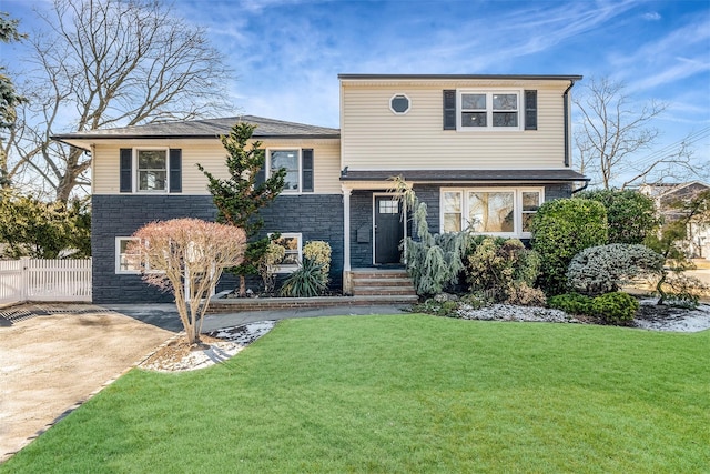 split level home featuring stone siding, driveway, a front lawn, and fence