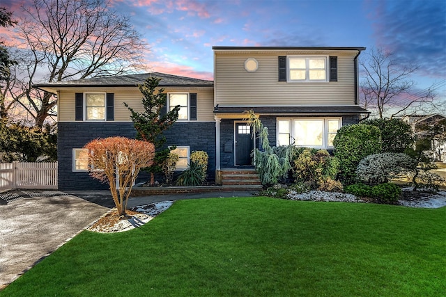 tri-level home with stone siding, a lawn, concrete driveway, and fence