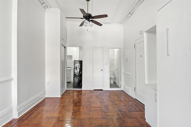 interior space with ceiling fan, dark parquet floors, crown molding, and a high ceiling