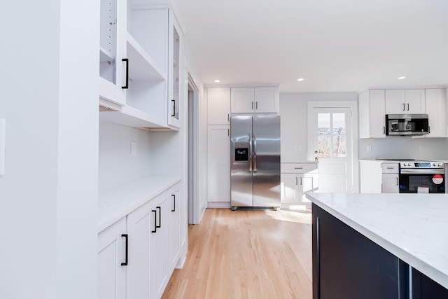 kitchen with light stone countertops, white cabinets, light hardwood / wood-style floors, and appliances with stainless steel finishes