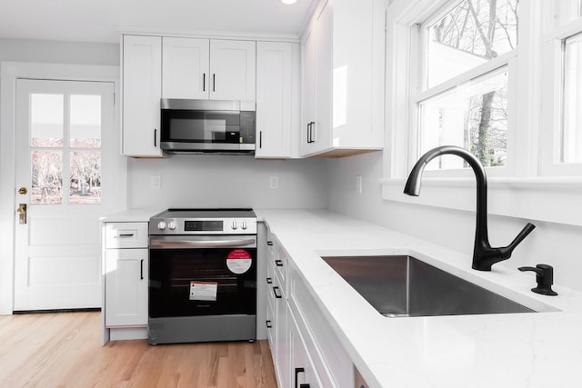 kitchen with white cabinetry, sink, stainless steel appliances, light stone counters, and light hardwood / wood-style floors