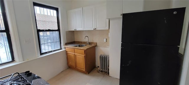 kitchen featuring radiator, white cabinets, black refrigerator, sink, and light tile patterned floors