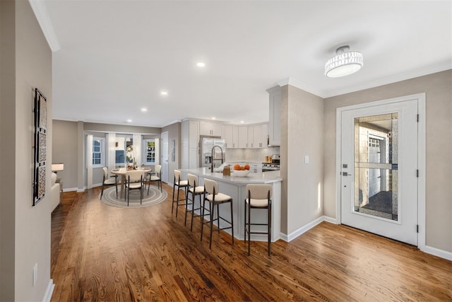 kitchen with white cabinetry, dark hardwood / wood-style flooring, kitchen peninsula, a breakfast bar, and appliances with stainless steel finishes