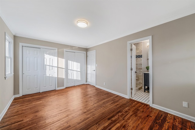 unfurnished bedroom featuring hardwood / wood-style flooring, ensuite bathroom, ornamental molding, and multiple closets