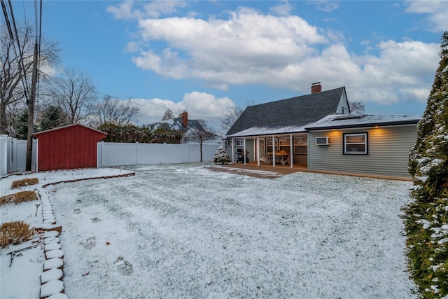 snowy yard with covered porch, a shed, and a wall mounted AC