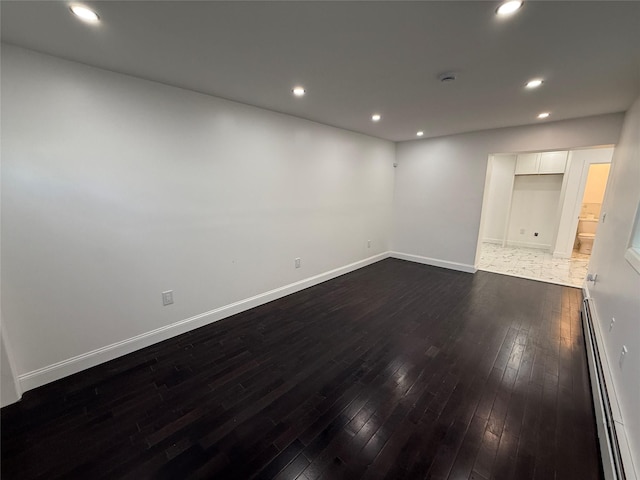 empty room featuring dark wood-type flooring and a baseboard heating unit